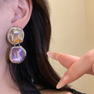 Detailed on-ear view of luxury silver needle earrings with purple and amber crystals