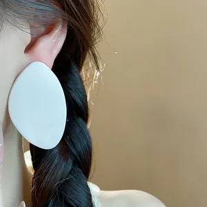 Vue détaillée de grandes boucles d'oreilles en résine blanche en forme de feuille.