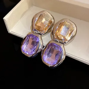 Close-up of elegant square earrings with purple and amber crystals in a gift box.