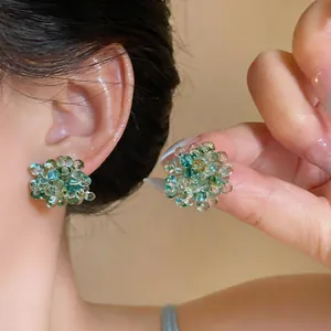 Detailed close-up of green glass beaded flower stud earrings being worn and held