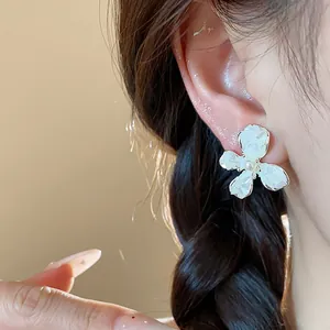 Dettaglio di eleganti orecchini a fiore con petali di smalto bianco e perla centrale