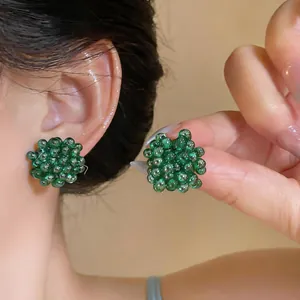Close-up of vibrant green glass beaded flower earrings worn on ear and held by hand.