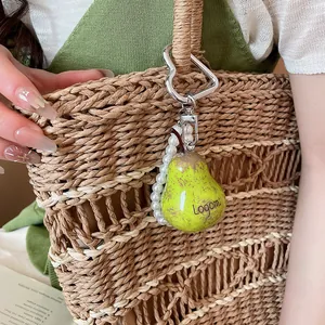 Close-up detail of a fresh green pear-shaped charm with pearl accents on a straw bag