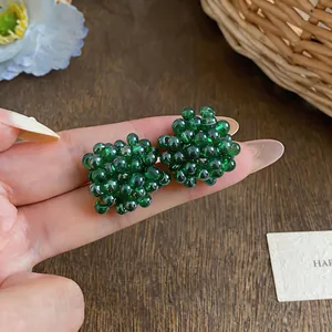 Detail macro of green glass beaded flower cluster stud earrings held in hand