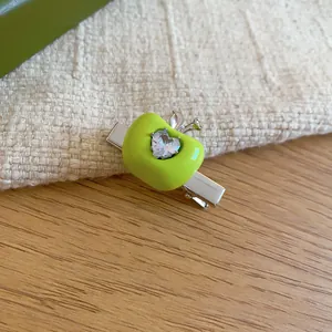 Close-up of a lime green apple hair clip with a sparkling heart-shaped gemstone detail