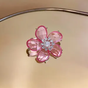 Detailaufnahme eines süßen rosa Zirkon-Blumen-Ohrclips auf einer goldenen Spiegelfläche.