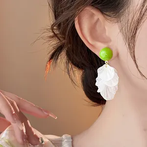 Primo piano di orecchini in acrilico verde con nappe di petali bianchi indossati dalla modella
