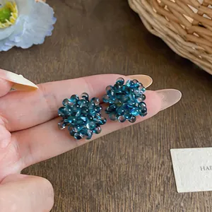Detailed macro view of blue glass beaded flower cluster stud earrings held by hand