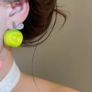 Close-up of a vibrant green bitten apple stud earring with sparkling rhinestone leaf detail