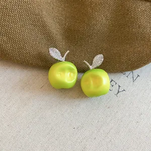 Close-up of green apple earrings with sparkling leaf detail on linen background.