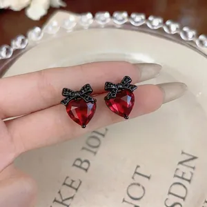 Elegant red heart-shaped stud earrings with black bow detailing displayed on a plate