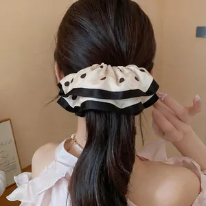 Detail of a white polka dot scrunchie with black ruffled edges worn on a ponytail.