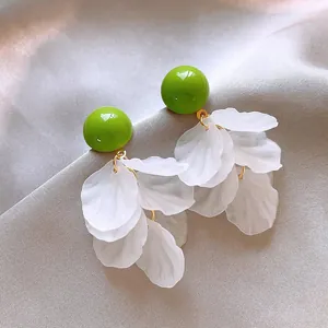 Primo piano di eleganti orecchini in acrilico verde con nappe di petali bianchi su tessuto