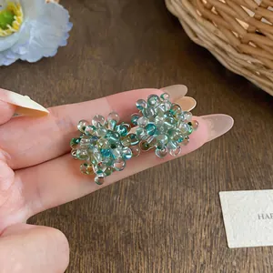 Close-up detail of handcrafted teal glass beaded flower earrings held on a hand