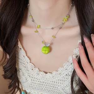 Close-up of a double-layered necklace with a vibrant green apple pendant and clear beads