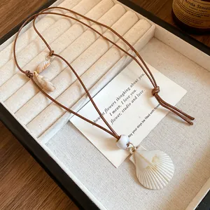Detailed view of beach-themed shell necklace with scallop pendant on brown cord cord.