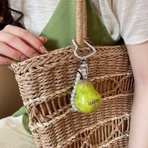 Detail view of a Mori style pear charm with pearls attached to a woven straw bag
