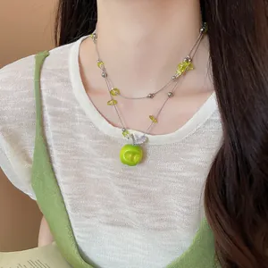 Detail of a forest-style double-layered necklace with a vibrant green apple pendant