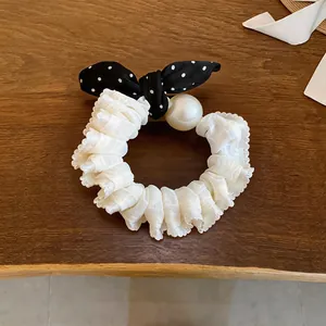 Close-up of a white ruffled scrunchie with a black polka dot bow and a faux pearl.