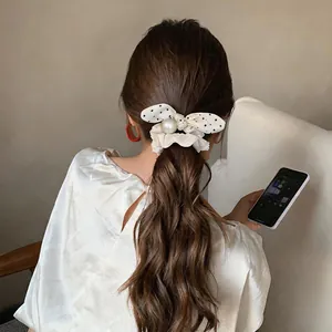 Close-up detail of a cream polka-dot bow scrunchie with a large pearl on a wavy ponytail