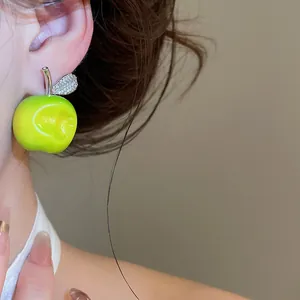 Close-up detail of a fresh green apple stud earring with a sparkling leaf on a model
