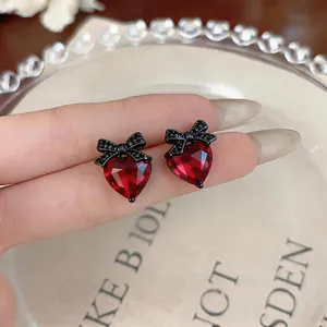 Close-up of elegant red heart stud earrings with black bow detail and cubic zirconia