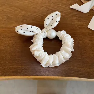 Detail view of the elegant white polka dot bow hair scrunchie featuring a large pearl