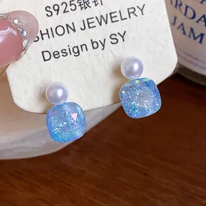 Macro detail of blue iridescent square glass stud earrings with pearl top on card