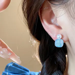 Close-up of elegant square blue glass and white pearl stud earring on ear.