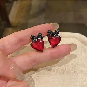 Close-up macro view of red heart zircon stud earrings featuring elegant black bow accents