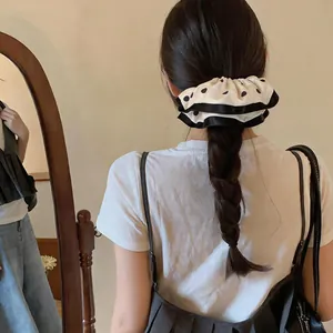 Polka dot fabric hair scrunchie with black lace trim shown on a braided ponytail
