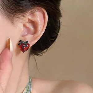Close-up of elegant red heart-shaped zircon stud earring with black bow-knot on ear