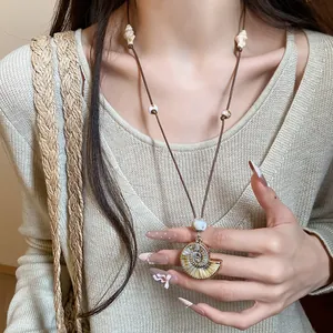Close-up of a vacation style seashell pendant necklace on a beige knit top