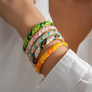 Detalle de brazaletes de metal esmaltado de colores apilados en la muñeca, estilo dopamina