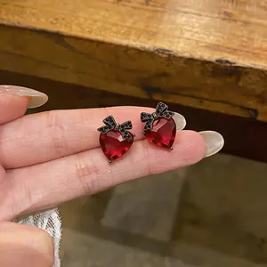 Close-up detail of red heart zircon stud earrings with black bow accents in silver