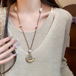 Detailed shot of a nautilus seashell pendant necklace on a beige knit sweater