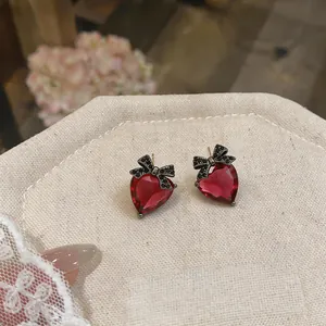 Close-up detail of heart-shaped red gemstone earrings with black zirconia bow design