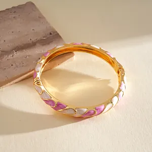 Detalle de brazalete dorado con ondas y esmalte rosa y blanco de colores vibrantes.