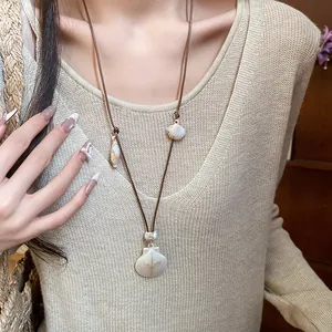 Close-up of beach vacation shell necklace jewelry on model wearing beige knit top