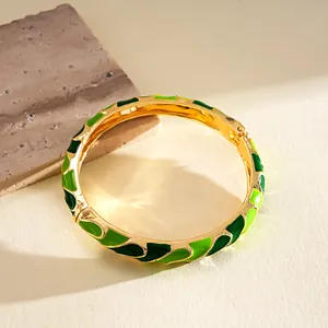 Vista detallada del patrón de esmalte verde en un brazalete rígido de tono dorado.