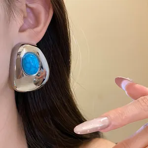 Close-up of vintage chunky silver stud earrings with blue resin center on model's ear