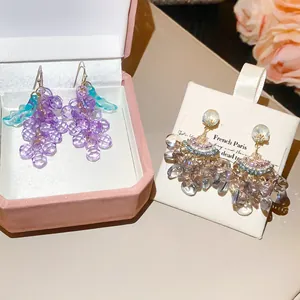 Détail des boucles d'oreilles en grappe de raisin violette et pompon en forme d'éventail
