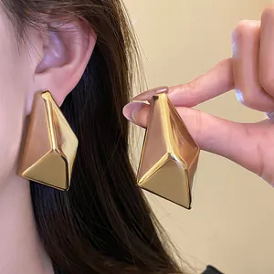 Nahaufnahme goldener unregelmäßiger geometrischer Ohrstecker an einem Modell.