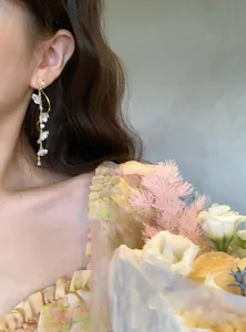 Detail of elegant long tassel earrings with white floral elements and gold-tone finish