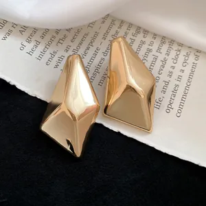 Makroaufnahme minimalistischer unregelmäßiger geometrischer Goldohrstecker auf Zeitung