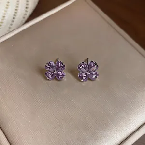 Detailed macro view of purple flower-shaped zircon stud earrings on a beige jewelry box