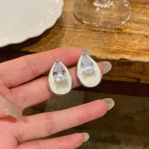 Close-up detail of silver teardrop stud earrings with clear zircon and white enamel