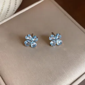 Close-up detail of elegant light blue zircon flower stud earrings on a beige texture