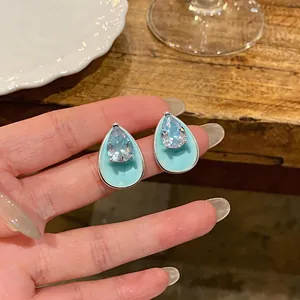 Detailed hand-held view of silver needle water-drop earrings with mint enamel and zircon.
