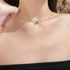 Close-up of a minimalist silver choker necklace with a brilliant blue heart pendant